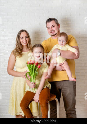 Funny Family Portrait auf Ostern von Mutter, Vater und Kinder tragen gelbe Kleidung und gegen weiße Wand posieren Stockfoto