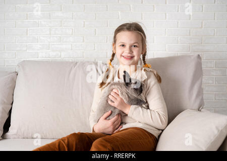 Portrait von glücklichen Mädchen mit Hase sittiing auf dem Sofa im Wohnzimmer. Stockfoto