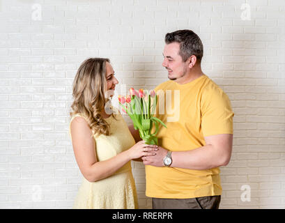 Junger Mann und Frau mit Tulpen und tragen gelbe Kleidung gegen weiße Wand Stockfoto