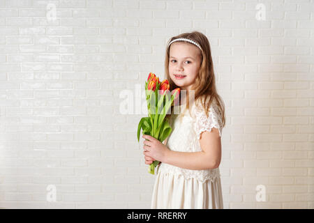 Kleines Mädchen mit langen blonden Haaren, die in weißem Kleid mit Tulpen auf weißem Hintergrund Stockfoto