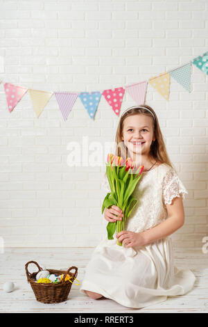 Kleine Mädchen in weißem Kleid mit Tulpen auf Ostern Hintergrund Stockfoto