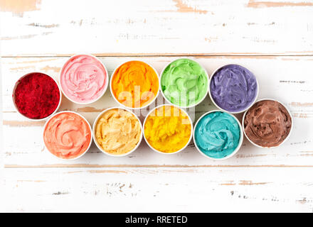 Viele Tassen mit bunten Regenbogen Eis auf weißem Holz- Hintergrund. Ansicht von oben Stockfoto