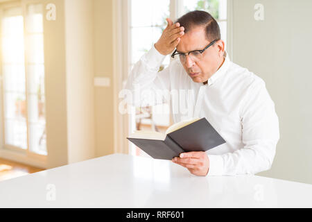 Mittleres Alter Mann ein Buch zu Hause lesen Brille mit Hand betonte am Kopf, mit Scham und Überraschung Gesicht schockiert, wütend und frustriert. Angst und Stockfoto