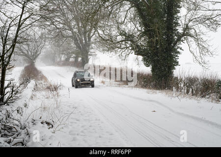 Der Dacia Duster Fahrt auf einer verschneiten Landstraße nahe Eastleach. Cotswolds, Gloucestershire, England Stockfoto