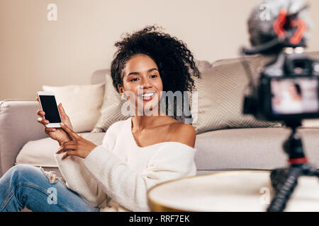 Weibliche vlogger Holding Smartphone während der Videoaufnahme im Wohnzimmer Stockfoto