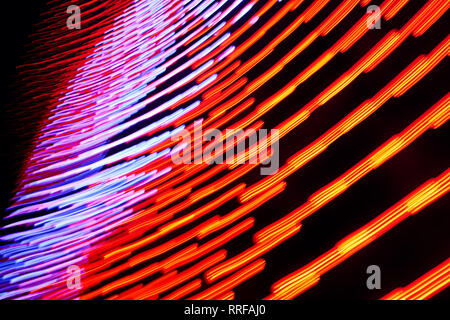 Rot-orange und blau-violett leuchtende Linien in Bewegung auf dem dunklen Hintergrund. Closeup horizontale Foto. Stockfoto