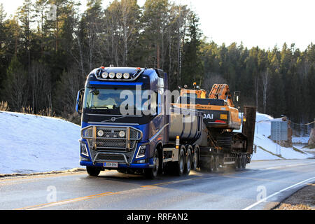 Salo, Finnland - 24. Februar 2019: Blaue Volvo FH Truck von M. Toivonen Oy hols Huyndai Robex LC300 Raupenbagger am Anhänger entlang der Straße im Winter. Stockfoto