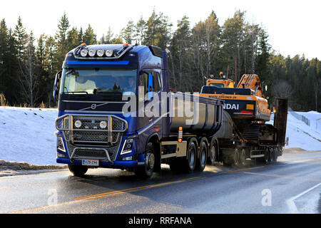 Salo, Finnland - 24. Februar 2019: Blaue Volvo FH Truck von M. Toivonen Oy hols Huyndai Robex LC300 Raupenbagger am Anhänger entlang der Straße im Winter. Stockfoto