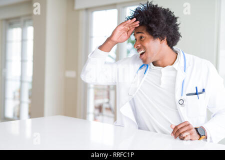 Afrikanische amerikanische Arzt Mann in der Klinik sehr glücklich und lächelnd weit entfernt, mit der Hand über den Kopf. Suche Konzept. Stockfoto