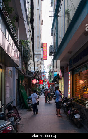 Eine enge Gasse mit Läden und Restaurants gesäumt von Menschen gehen vorbei, Hanoi, Vietnam Stockfoto