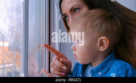 Junge Mutter und nachdenkliche kleine Junge Blick durch Fenster Stockfoto