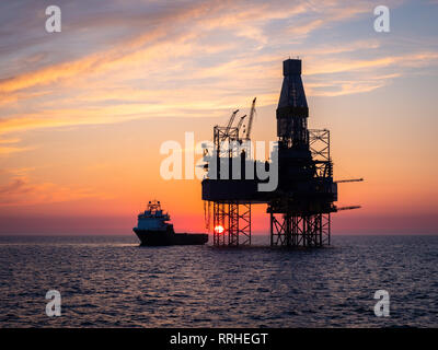 Eine Ölplattform in der Nordsee mit einem Versorgungsschiff neben während des Sonnenuntergangs.