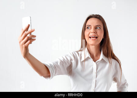 Spaß haben. Frau, die isoliert auf weißem Unter selfie auf dem Smartphone Grimassen zu Kamera Stockfoto