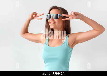 Freestyle. Frau in Sonnenbrille ständigen Studio auf weissem, Frieden Geste isoliert toothy Lächeln Stockfoto