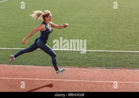 Sportlicher Lifestyle. Junge Frau auf Stadion läuft bestimmt Seitenansicht Stockfoto