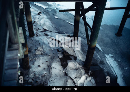 Gefrorenes Wasser und kalte Eis Risse unter Druck sowie eine Marina Ufer neben einem Bootsdock. Stockfoto