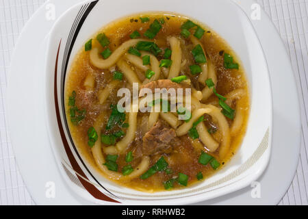 Schüssel mit Miso Suppe mit Udon-nudeln, Kohl, Schweinefleisch und grüne Zwiebeln mit Stäbchen auf einem Bambus Serviette Stockfoto