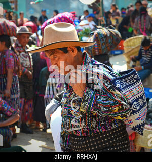 Porträt eines Mannes in traditioneller Kleidung auf dem Solola-Markt mit maya-Leuten im Hintergrund, die Waren kaufen und verkaufen, Guatemala. Stockfoto