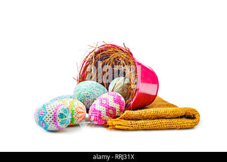 Bunte Ostereier aus Nest in den roten Eimer mit Stoff auf weißem Hintergrund verschüttet. Frohe Ostern Stockfoto