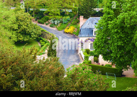 Blick auf die kleine Stadt Augustins, Frankreich. Weißes Haus mit grauen Dach inmitten von grünen Bäumen und Blumen. Bewölkt Frühlingstag. Von oben geschossen Stockfoto