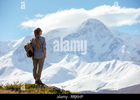 Frau mit Rucksack steht auf Sicht und blickt auf die Berge Stockfoto