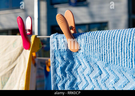 Orange Wäscheklammer hält blau Handtuch auf der Wäscheleine im Hinterhof. Stockfoto