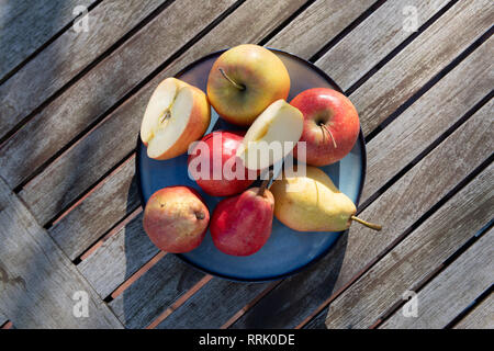 Birnen und Äpfel auf blauen Platte im Sonnenlicht auf hölzernen Tisch. Stockfoto