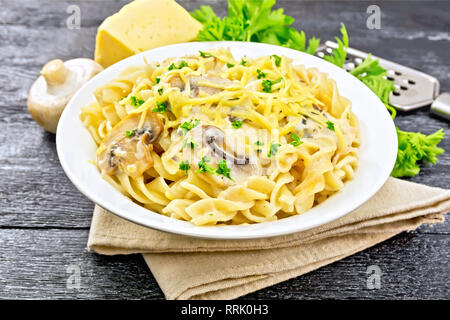 Fusilli mit Champignons in Rahmsauce, Petersilie und geriebenem Käse in einer Platte auf Serviette auf Holzbrett Hintergrund Stockfoto