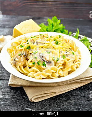 Fusilli mit Champignons in Rahmsauce, Petersilie und geriebenem Käse in einer Platte auf Serviette auf dem Schwarzen Brett Hintergrund Stockfoto