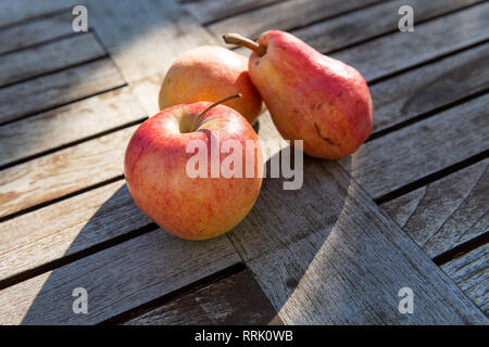 Zwei rote und gelbe Birnen und ein Apple liegen auf einem rustikalen Garten Tisch in der Sonne. Stockfoto