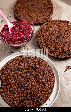 Schritte bei der Herstellung von Schokolade Kuchen. Keks Schichten auf Papier und kirschfüllung Für die Herstellung von Kuchen. Stockfoto