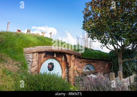 Hobbiton movie, Matamata, Neuseeland. . Malerische kleine Hobbit Haus mit blauer Tür, in einer grünen Hügellandschaft und blauer Himmel Stockfoto