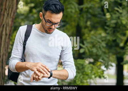 Portrait von Smart verantwortlichen Mann mit modernen Frisur schaut auf eine Wand am Handgelenk über verschwommenes Park Hintergrund beeilen Sie sich für das Treffen. Management employmen Stockfoto