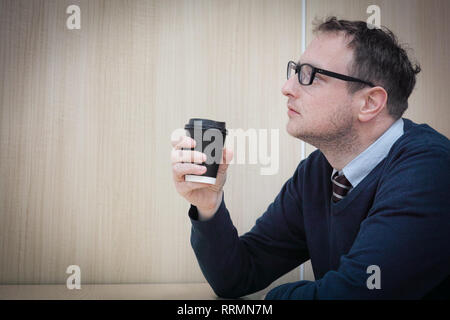 Ein Mann schaut nachdenklich während seiner Pause während seinen Kaffee trinken. Stockfoto