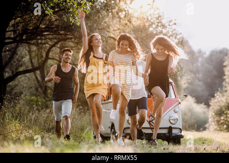 Eine Gruppe junger Freunde vor der retro Minivan auf einem Roadtrip durch Landschaft, springen. Stockfoto