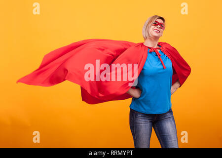 Junge und schöne blonde Frau gekleidet wie Superheldin mit rotem Umhang in der Luft. Rote Maske. Frau Superkräfte. Rote Maske. Stockfoto