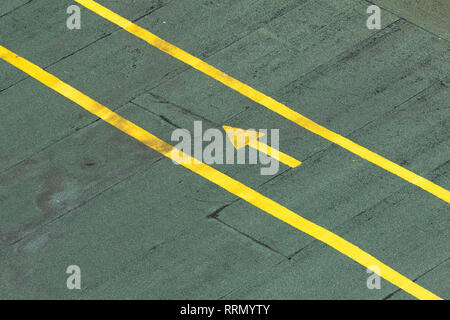 Gerichteter Verkehr gelber Pfeil auf einem grünen Tarmac Textur Stock Stockfoto