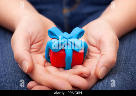 Frau hält Geschenk mit blauer Schleife umwickelt. Geschenkbox und Band sind aus Lehm gemacht (Knetmasse). Stockfoto