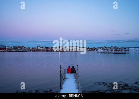 Paar am Rande der schneebedeckten Pier mit Blick auf die Waterfront Fischerdorf, Reine, Lofoten, Norwegen Stockfoto