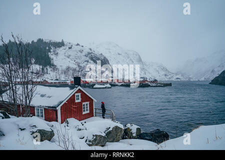 Frau genießen Sie ruhige Snowy Mountain View waterfront Fischerdorf, Lofoten, Norwegen Stockfoto