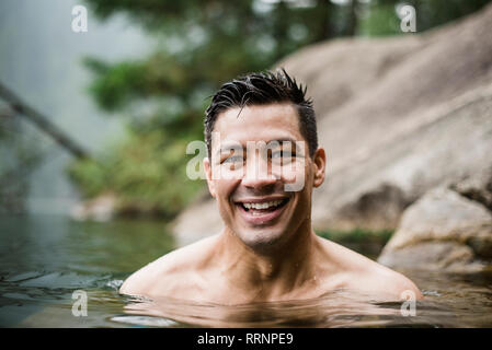 Porträt Lächeln, hübscher junger Mann Schwimmen im See Stockfoto