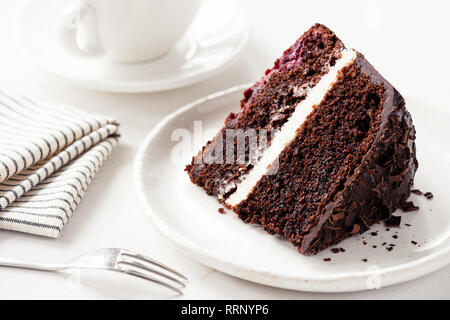 Schokoladenkuchen mit Sahne füllen. Stück dunkle Schokolade Kuchen auf weiße Platte. Geburtstagskuchen Stockfoto
