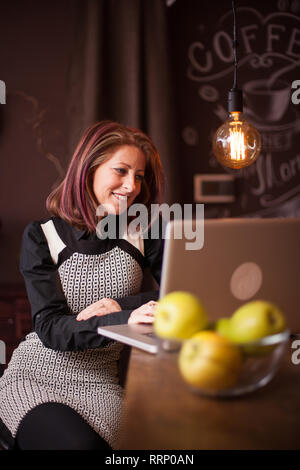 Geschäftsfrau, Lächeln, während Sie ihr Laptop in einem vintage Coffee Shop suchen. Genießen selbst beim Sitzen an der Theke Stockfoto