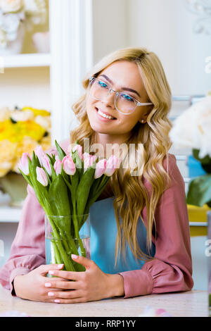 Schöne weibliche Blumenhändler in Gläsern und lächelnd Vase mit rosa Tulpen in Blüte shop Stockfoto