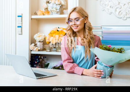 Schöne weibliche Blumenhändler in Gläsern sitzen mit floralen Bouquet am Computer Schreibtisch in Flower Shop Stockfoto