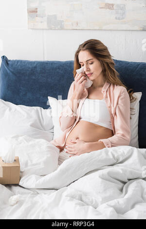 Schwangere Frau saß auf dem Bett und wischte sich mit Serviette umgekippt Stockfoto