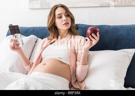 Schwangere Frau mit roten Apfel und Schokolade Stockfoto