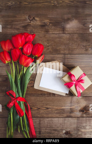 Kaffeebecher mit Bouquet von roten Tulpen und Notizen und Geschenk auf rustikalen Tisch von oben, schönes Frühstück, vintage Karte, Ansicht von oben, flach Stockfoto