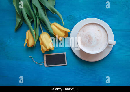 Kaffeebecher mit gelben Tulpen Blumen und Hinweise auf Blau rustikal Tabelle von oben, Frühstück am Muttertag oder Tag der Frauen Stockfoto