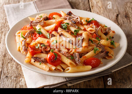 Leckeres Essen Nudeln mit gebackenen zog Schweinefleisch, Tomaten und Kräutern close-up auf einem Teller auf den Tisch. Horizontale Stockfoto